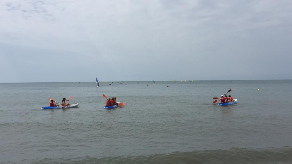 Grupos de personas con chalecos salvavidas reman en kayaks sobre aguas tranquilas, disfrutando de una actividad náutica al aire libre