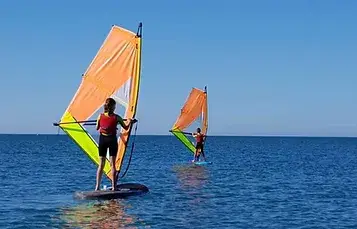 Dos personas practicando windsurf en el mar frente a la costa de Islantilla.