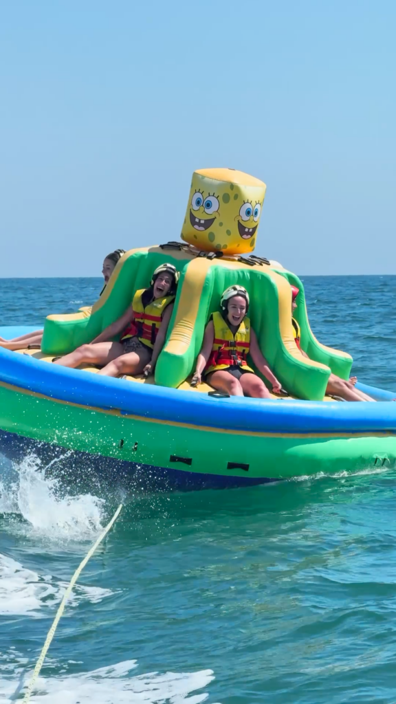 Jóvenes disfrutando de una atracción acuática hinchable en la playa de Islantilla, actividades náuticas en Huelva