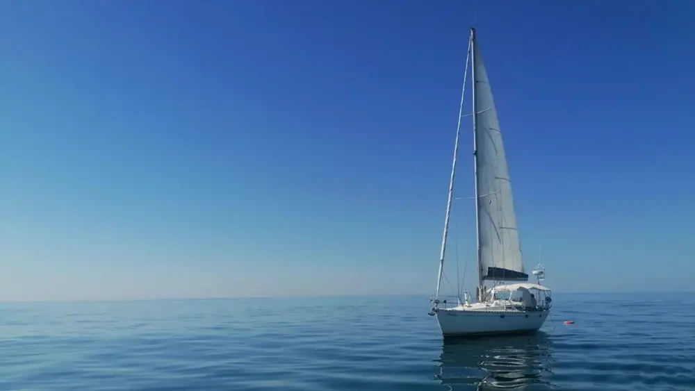Velero de Faro del Sur navegando frente a la costa de Isla Cristina en un día despejado.